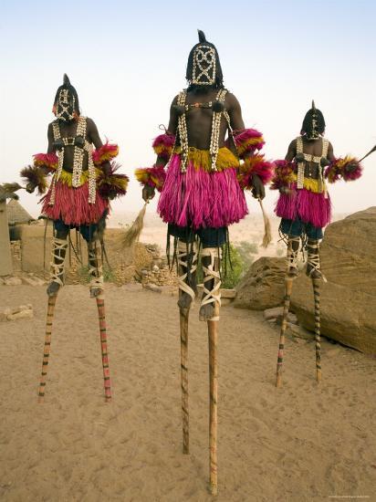 Traditional Dogan masked stilt dancers in colorful costumes over sandy landscape