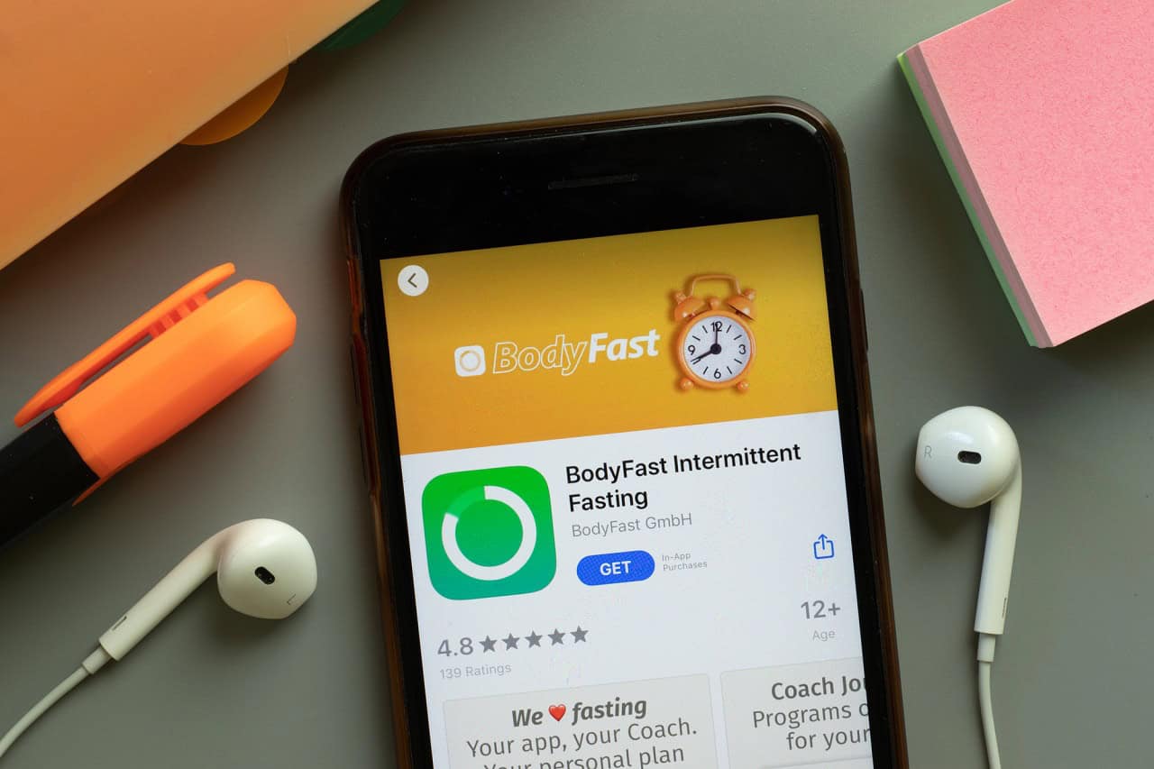 Fasting Faster intermittent fasting app listing on smartphone with earbuds and highlighter.