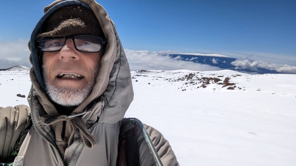 Hiker taking a selfie on a snowy mountain plateau under a bright blue sky