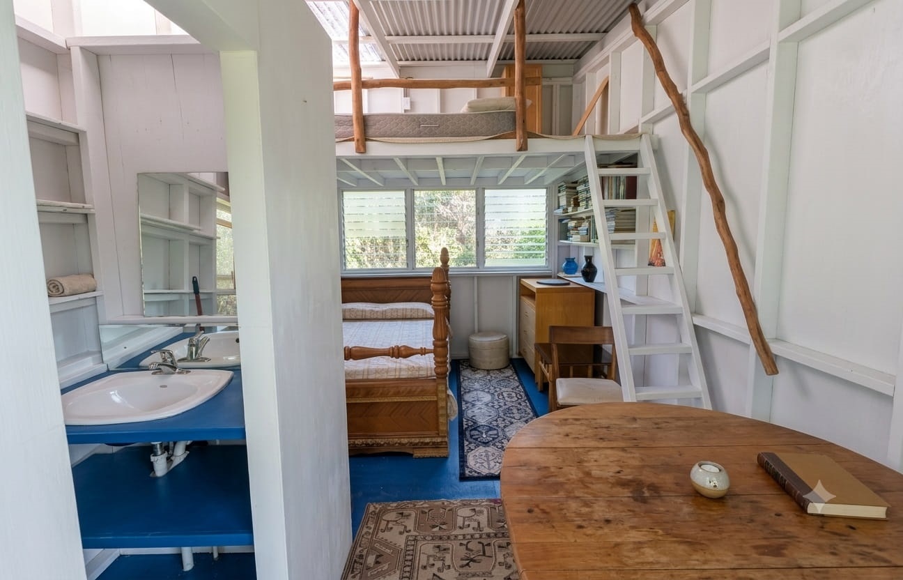 Bright tiny house studio with loft bed, ladder, bookshelves, twin bed, and sink vanity by large windows
